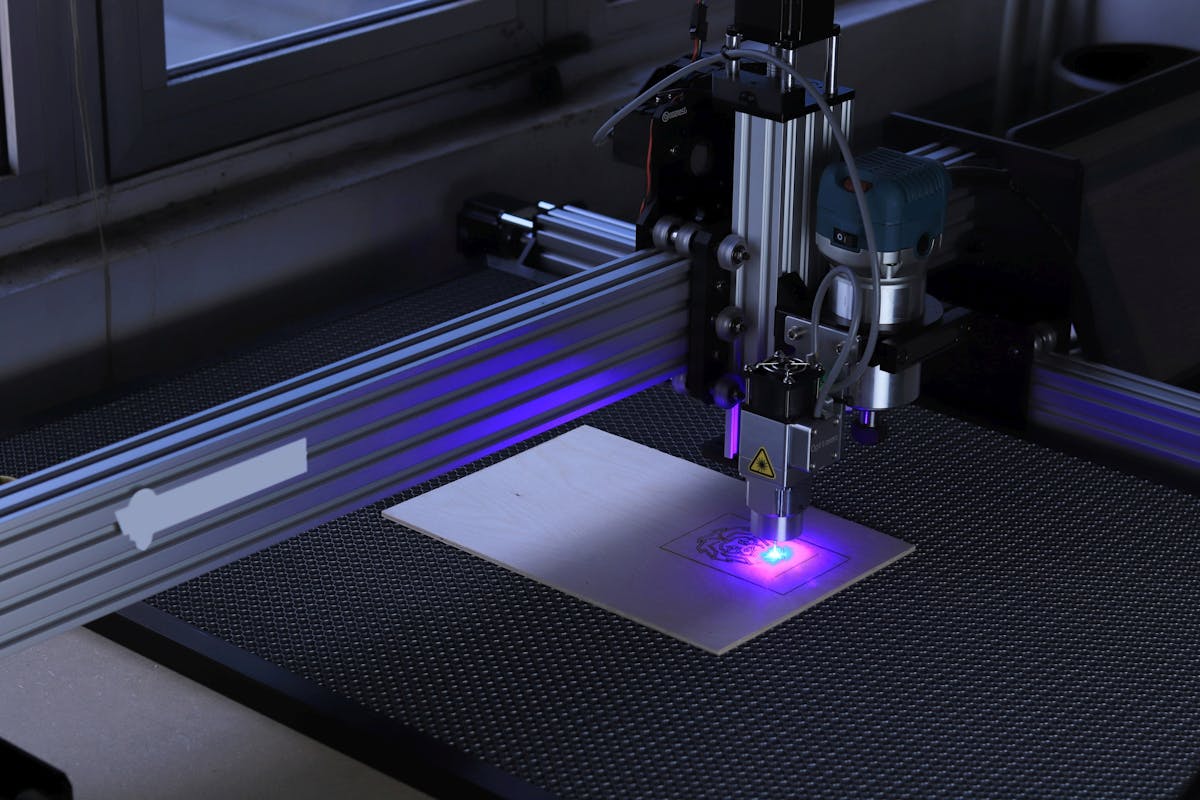 Close-up of a desktop laser engraving machine in operation with a visible blue laser beam.